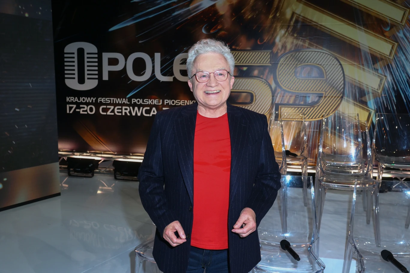 Felicjan Andrzejczak odszedł rok temu Starszy mężczyzna w okularach, ubrany w czerwony t-shirt i ciemną marynarkę, stoi na tle scenografii festiwalu Opole 59 z widoczną nazwą wydarzenia oraz datą.