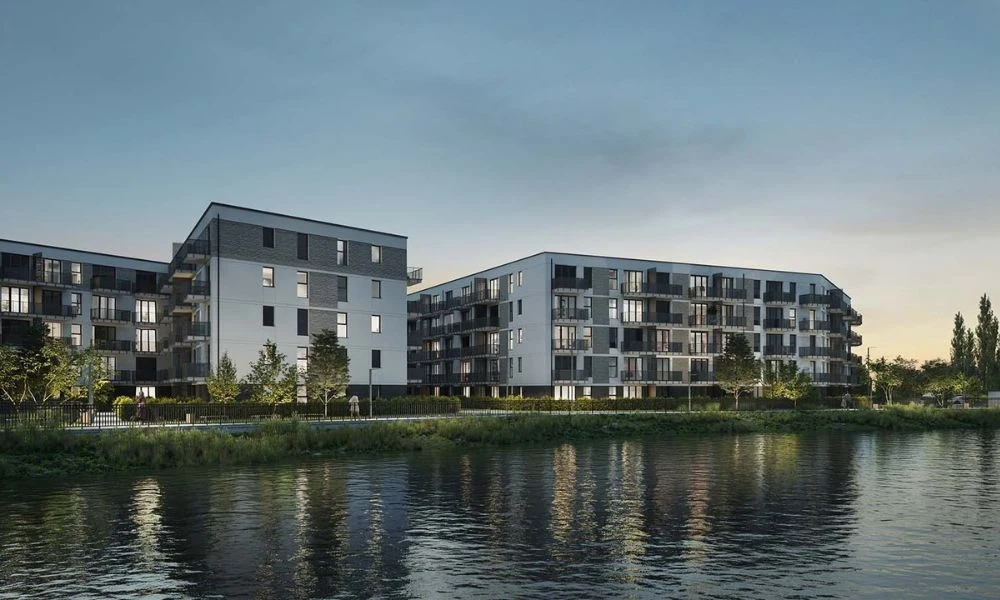 Grupa Murapol zaprasza do swoich biur sprzedaży w 16 miastach w Polsce na Dzień Otwarty Nowoczesny budynek mieszkalny o kilku kondygnacjach z dużymi balkonami, zlokalizowany w otoczeniu zieleni tuż nad wodą, oświetlony miękkim światłem wieczoru, z odbiciem fasady w spokojnej tafli jeziora.