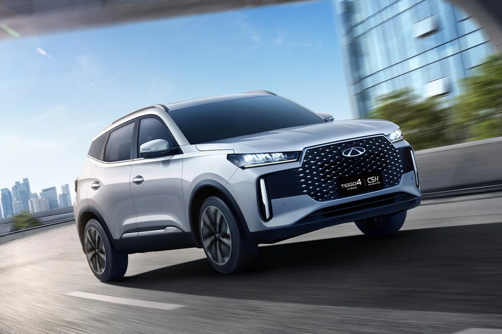 Nowoczesny, srebrny SUV marki Chery Tiggo 4 Pro w ruchu na tle miejskiej zabudowy, z widocznym dynamicznym grillem i charakterystycznym oświetleniem LED.