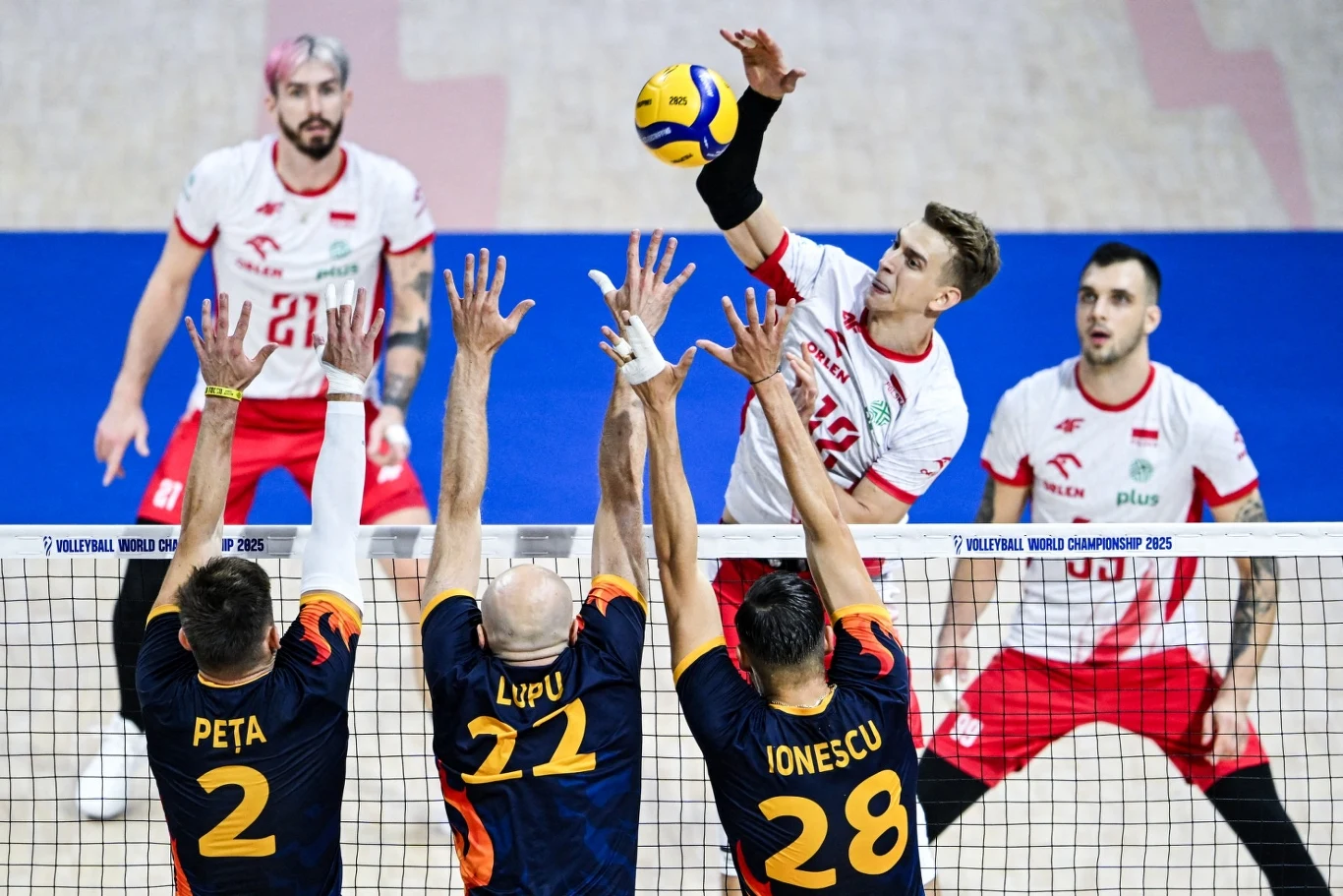 Znamy najlepszą szesnastkę MŚ na Filipinach Trzech siatkarzy w pomarańczowo-granatowych strojach próbuje zablokować atakującego zawodnika w biało-czerwonym stroju, który wykonuje wyskok do ataku nad siatką, a w tle widać dwóch kolejnych zawodników jego drużyny.