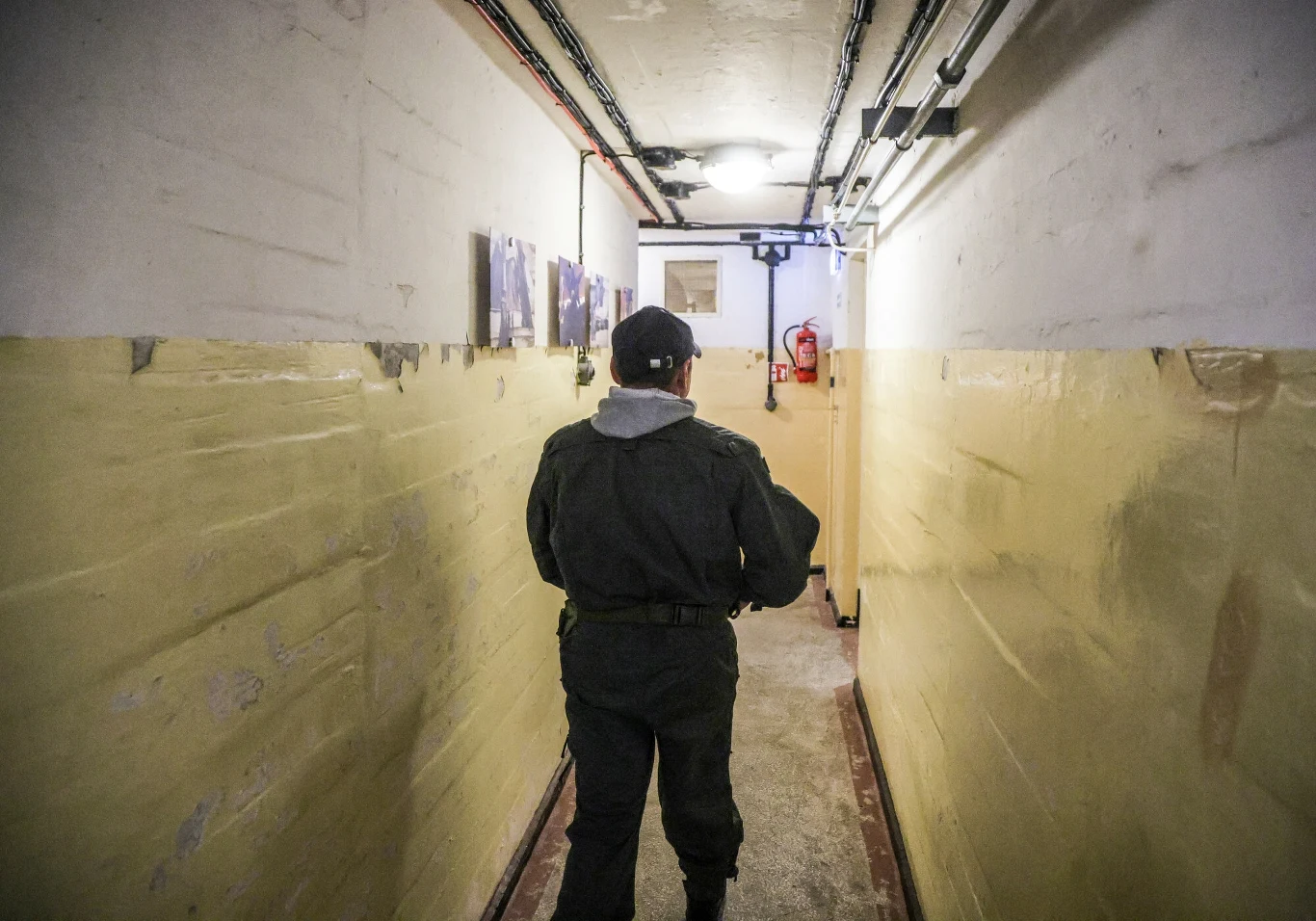 Polski rząd przeznacza ogromne pieniądze na remonty i budowę schronów dla ludności cywilnej. Na zdj. nieczynny od lat schron wojskowy pozostawiony na Pomorzu przez... Rosjan Człowiek w mundurze idący wąskim, surowym korytarzem o żółtych ścianach, na których wiszą kilka zdjęć lub plakatów, pod sufitem widoczne instalacje elektryczne.