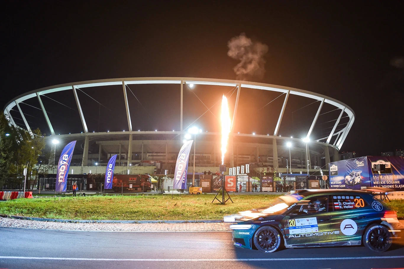 Rajd Śląska 2025 ponownie przejedzie ulicami Katowic Samochód rajdowy przejeżdżający obok stadionu podświetlonego nocą, z efektami pirotechnicznymi i flagami sponsorów przed obiektem.