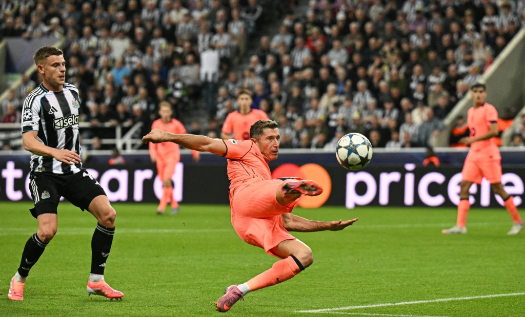 Po raz pierwszy w tym sezonie Robert Lewandowski znalazł się w wyjściowej jedenastce Barcelony Piłkarz w różowym stroju wykonuje dynamiczny wślizg do piłki w polu karnym podczas meczu na stadionie, w tle zawodnicy w czarno-białych strojach oraz tłum kibiców na trybunach.