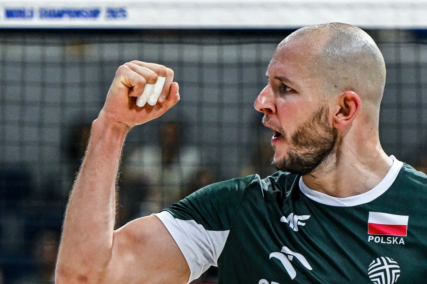 Bartosz Kurek emocjonująca scena sportowa z zawodnikiem siatkówki w zielonej koszulce z napisem 'Polska', gestykulującym zaciśniętą pięścią w wyrazie triumfu