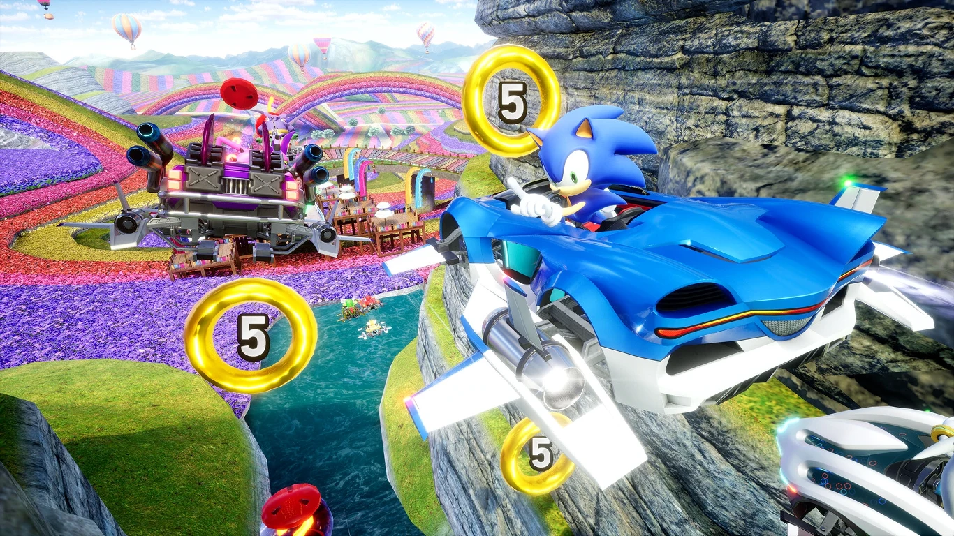 Sonic jedzie futurystycznym samochodem przez kolorowy, bajkowy tor wyścigowy, unosząc się nad przepaścią, wokół niego unoszą się złote monety z liczbą 5, w tle znajduje się fantazyjne otoczenie i kolorowe balony.