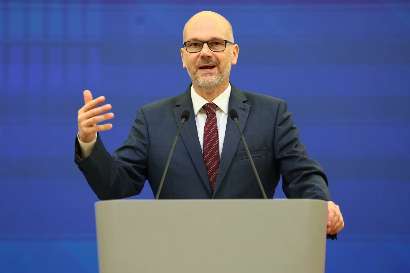 Maciej Berek przedstawił priorytety rządu na najbliższe lata Mężczyzna w okularach i garniturze, stojący za mównicą, gestykuluje podczas przemówienia na tle niebieskiej ściany.