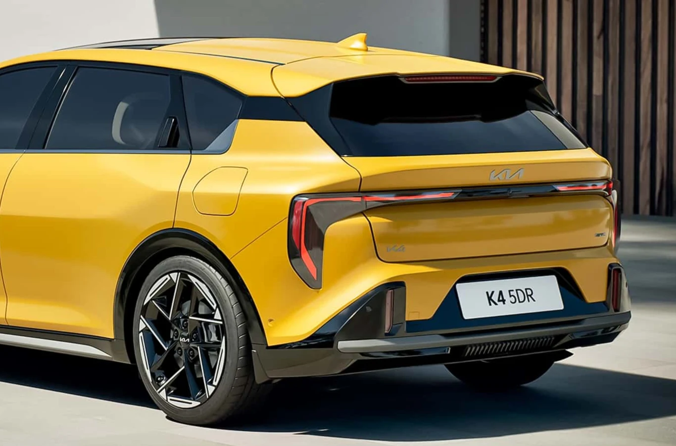 Jaskrawo żółty samochód marki Kia o nowoczesnym, dynamicznym designie, widoczny z tyłu, z charakterystycznym światłem LED w kształcie litery T, sportowymi felgami i oznaczeniem K4 5DR na tablicy rejestracyjnej.