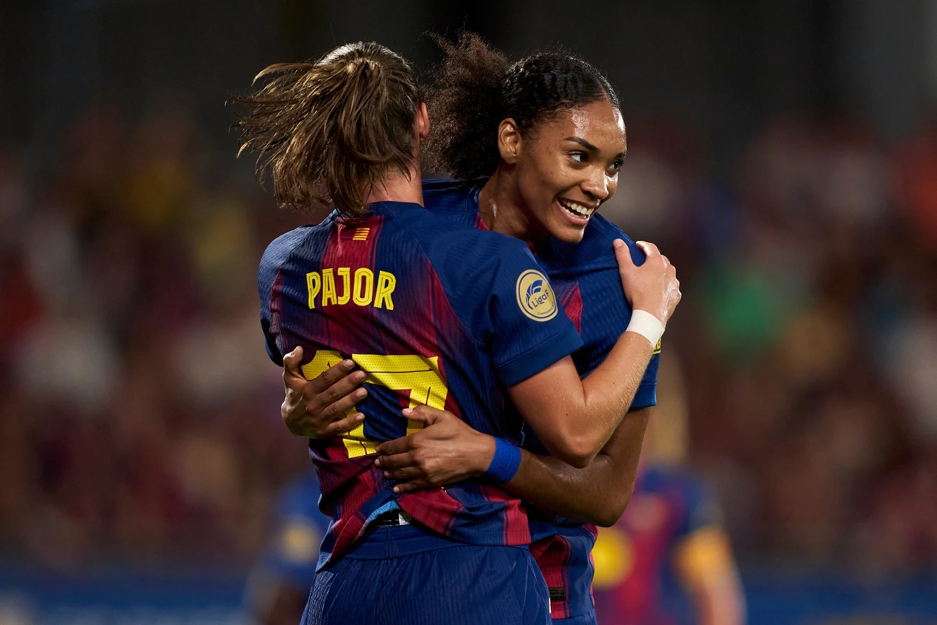 Dwie piłkarki w strojach klubowych przytulają się na boisku, jedna z nich zwrócona tyłem z widocznym napisem Pajor na koszulce, druga uśmiechnięta, atmosfera radości po zdobyciu gola lub zakończonej akcji.
