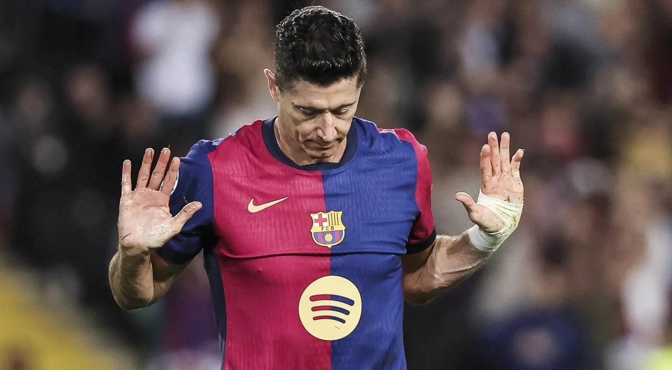 Robert Lewandowski Piłkarz w koszulce FC Barcelony z uniesionymi rękoma, bandażem na lewej dłoni i opuszczoną głową podczas meczu na stadionie.