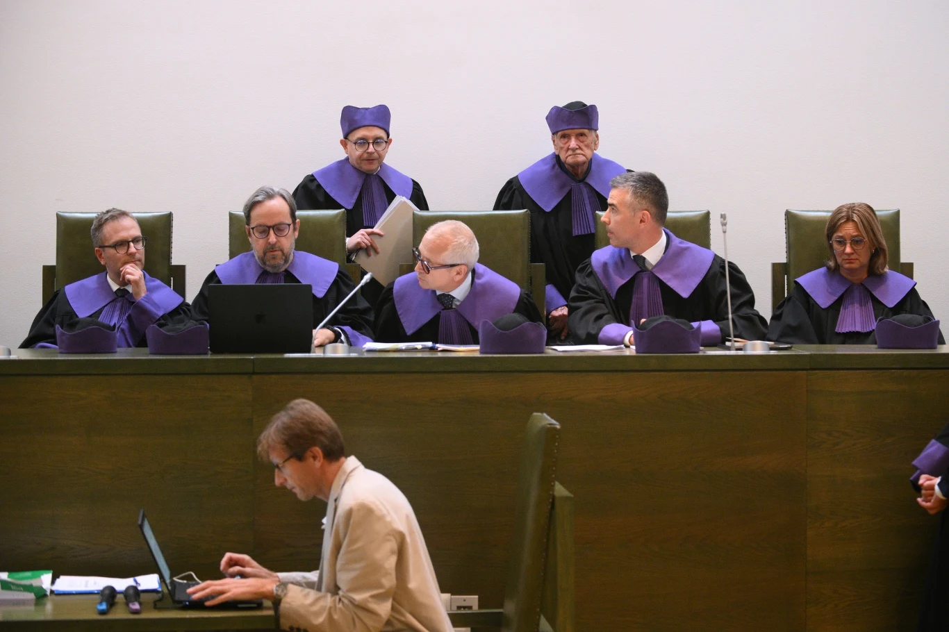 Trybunał Stanu zdecydował w sprawie Manowskiej Grupa sędziów ubrana w togi i birety siedzi przy stole sędziowskim, niektórzy analizują dokumenty lub pracują przy komputerach, z przodu mężczyzna z laptopem wykonuje notatki.