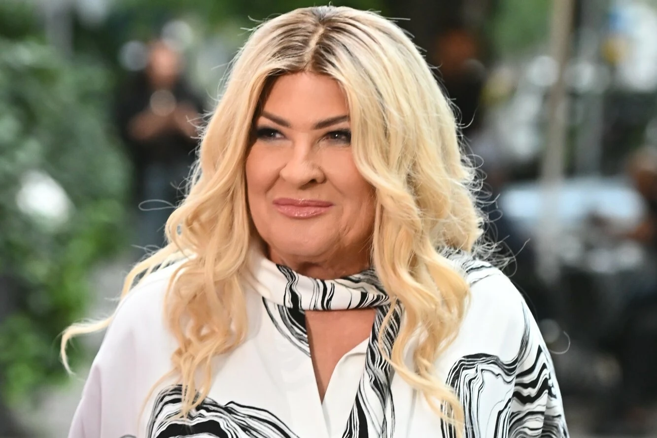 Beata Kozidrak rusza w jesienną trasę razem z Bajmem Kobieta o blond włosach ułożonych w fale, uśmiecha się lekko, ubrana w elegancką biało-czarną bluzkę z wzorem, na tle rozmytego zielonego tła.