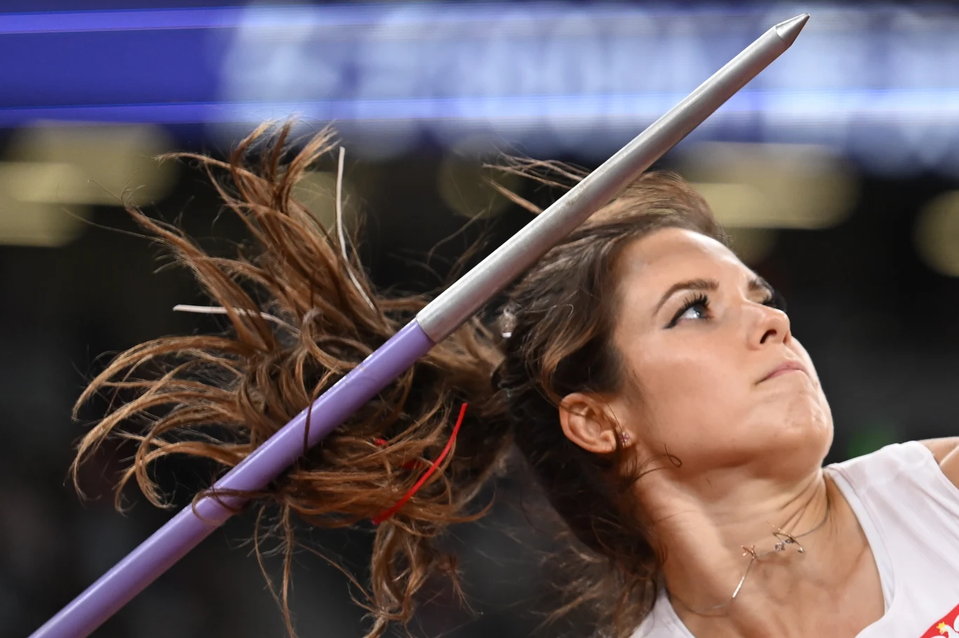 Maria Andrejczyk Sportowiec podczas dynamicznego rzutu oszczepem, skupiona twarz i rozwiane włosy podkreślają intensywność działania.