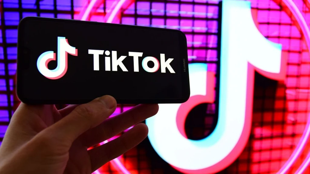 Los TikToka przesadzony po rozmowie Donalda Trumpa i Xi Jinpinga Logo TikTok wyświetlone na ekranie smartfona trzymanego w ręce na tle powiększonej wersji tego samego logo widocznej na kolorowej ścianie.