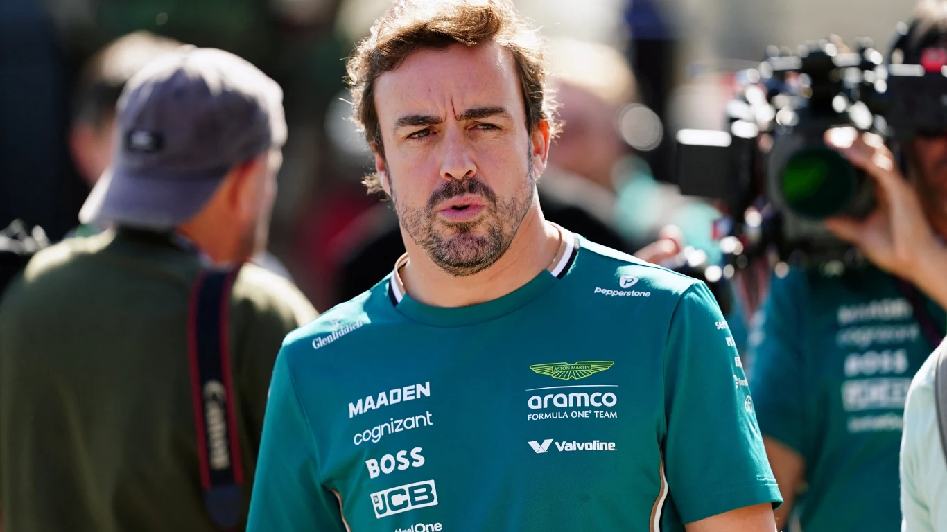 Mężczyzna w zielonej koszulce z logo sponsorów zespołu sportowego, w tle inni ludzie oraz profesjonalny sprzęt fotograficzny, scena uchwycona podczas wydarzenia sportowego.