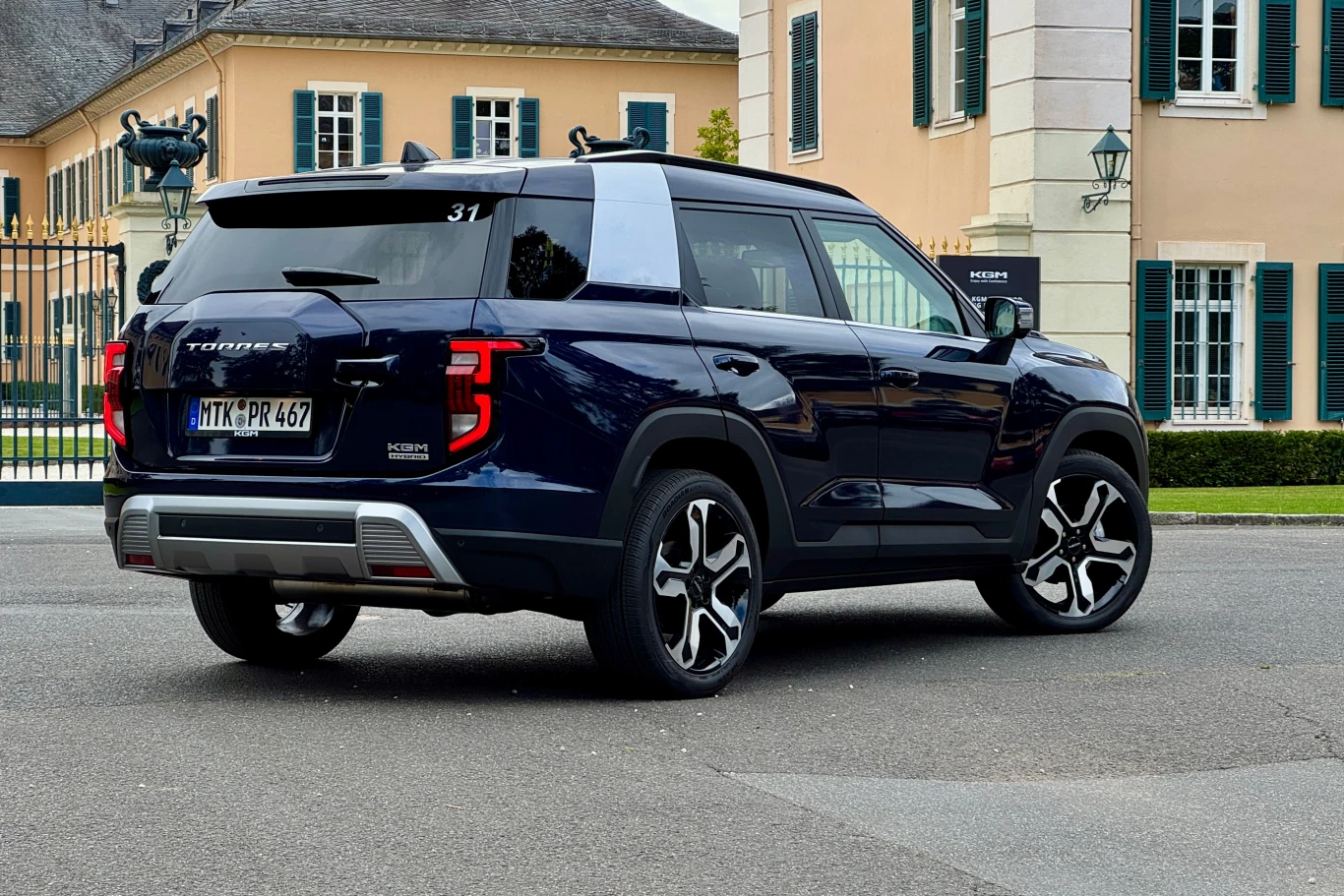 Granatowy SUV z nowoczesnym designem, masywnymi felgami oraz oznaczeniem TIVOLI na tylnej klapie stoi zaparkowany przy eleganckich budynkach z zielonymi okiennicami.
