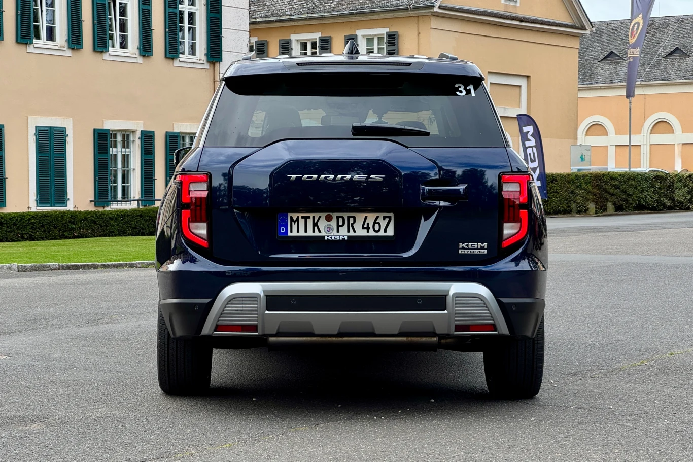 Granatowy samochód terenowy marki Torres zaparkowany tyłem na ulicy w otoczeniu eleganckich budynków o jasnych elewacjach i zielonych okiennicach.