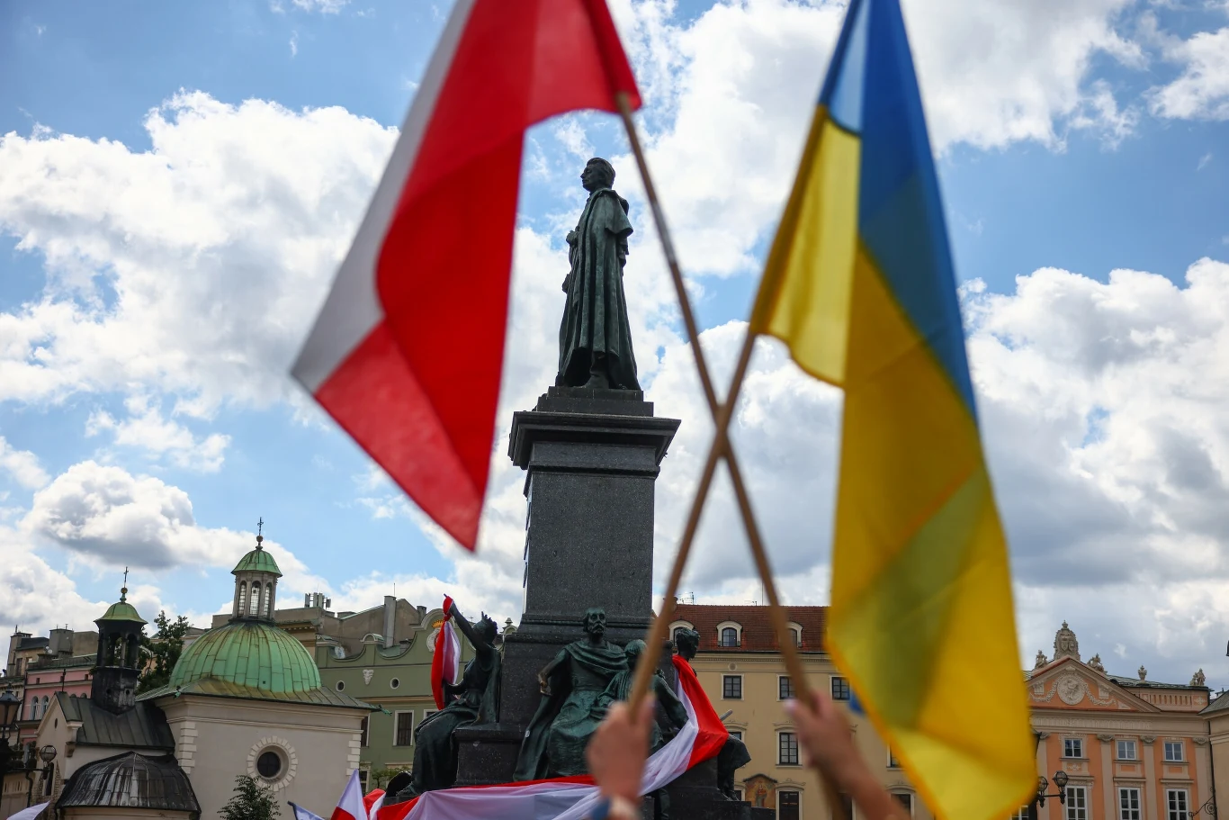 Jak Polacy oceniają obecność Ukraińców w naszym kraju? Jest najnowszy sondaż Pomnik Adama Mickiewicza w Warszawie na tle nieba, na pierwszym planie uniesione flagi Polski i Ukrainy trzymane przez zgromadzonych uczestników.