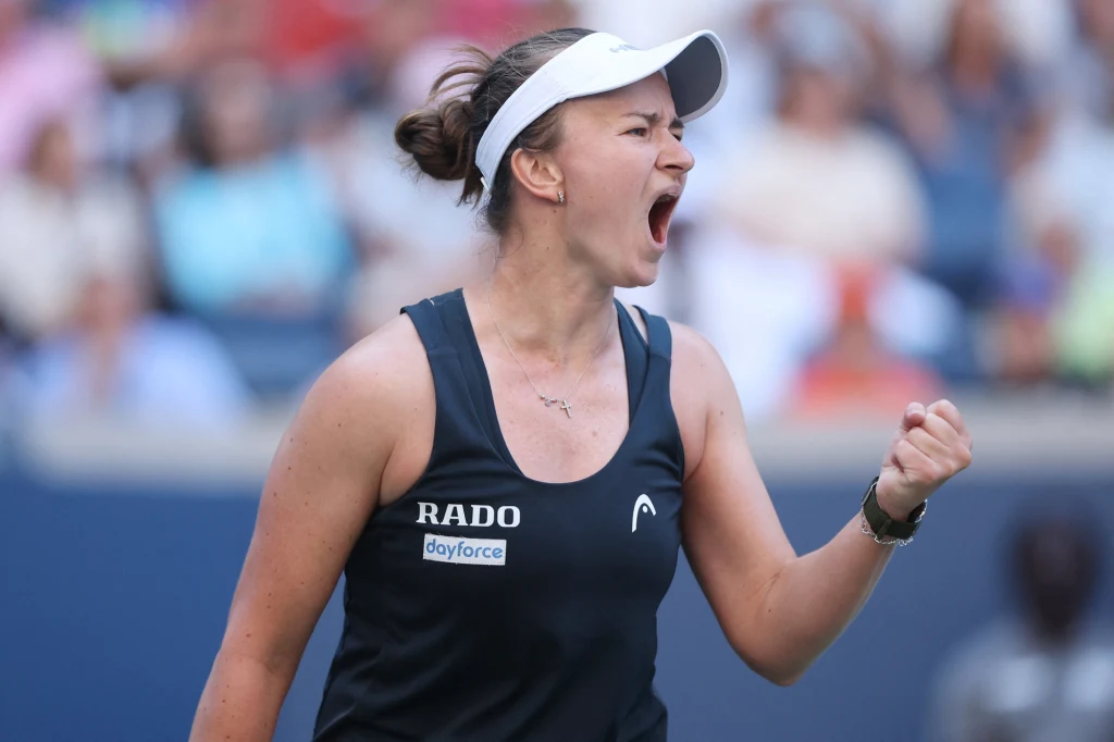 Barbora Krejcikova Zawodniczka tenisowa w czarnej koszulce i białej czapce wyraża silne emocje, zaciska pięść w geście triumfu na korcie tenisowym, widoczna publiczność w tle.