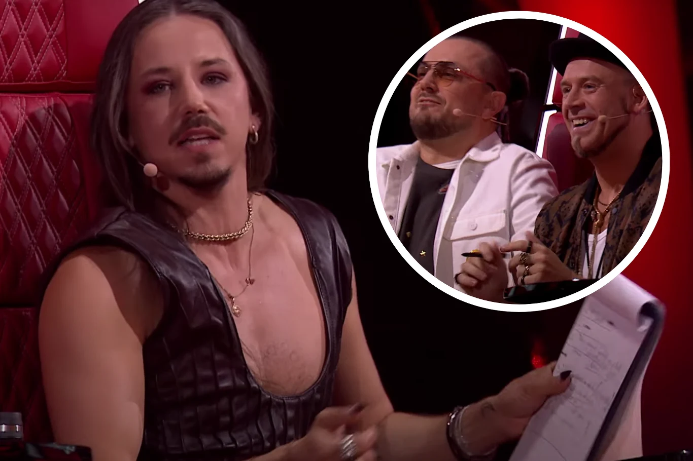 Michał Szpak oraz Tomson i Baron podczas Przesłuchań w Ciemno w "The Voice of Poland" Sędzia w efektownym stroju skórzanym z notatnikiem w ręku podczas telewizyjnego programu zasiada w czerwonym fotelu, na pierwszym planie; w kółku dwóch mężczyzn uśmiechających się i trzymających długopisy widocznych w tle programu, wszyscy są skupieni ...