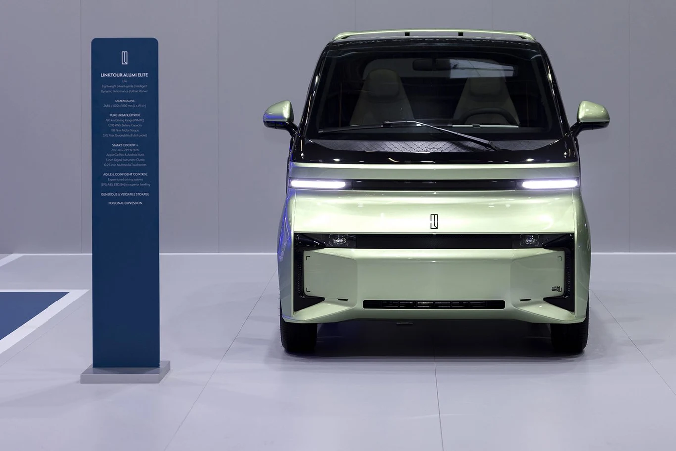 Nowoczesny samochód elektryczny ustawiony frontem na białym podłożu z panelową tablicą informacyjną obok pojazdu, minimalistyczny design, czyste linie i jasne oświetlenie podkreślające futurystyczny charakter auta.