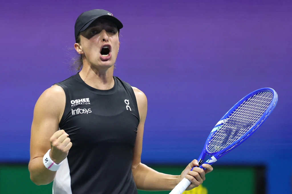 Iga Świątek Tenisistka w czarnej koszulce i czapce, trzymająca rakietę i zaciskająca pięść w geście triumfu, wyraża silne emocje podczas meczu.