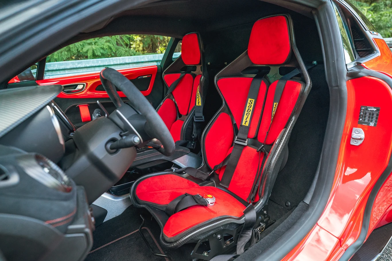 Kubełkowe fotele Sabelt z sześciopunktowymi pasami bezpieczeństwa to wyróżnik A110 R Wnętrze sportowego samochodu z wyraźnie widocznymi, czerwonymi kubełkowymi fotelami wykończonymi czarnymi akcentami i pasami bezpieczeństwa, elementy kokpitu oraz drzwi pokryte ciemnymi panelami