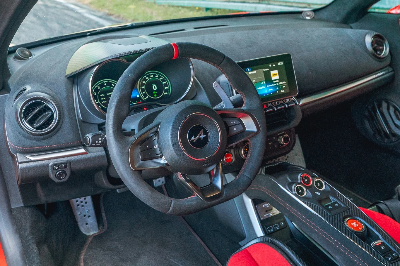 Deska rozdzielcza A110 R jest taka sama jak w pozostałych odmianach. Deskę rozdzielczą obito alcantarą Wnętrze nowoczesnego samochodu sportowego z widocznym logo Alpine na kierownicy, cyfrowym zestawem wskaźników, ekranem multimedialnym, sportowymi fotelami i wykończeniem alcantarą z czerwonymi akcentami.