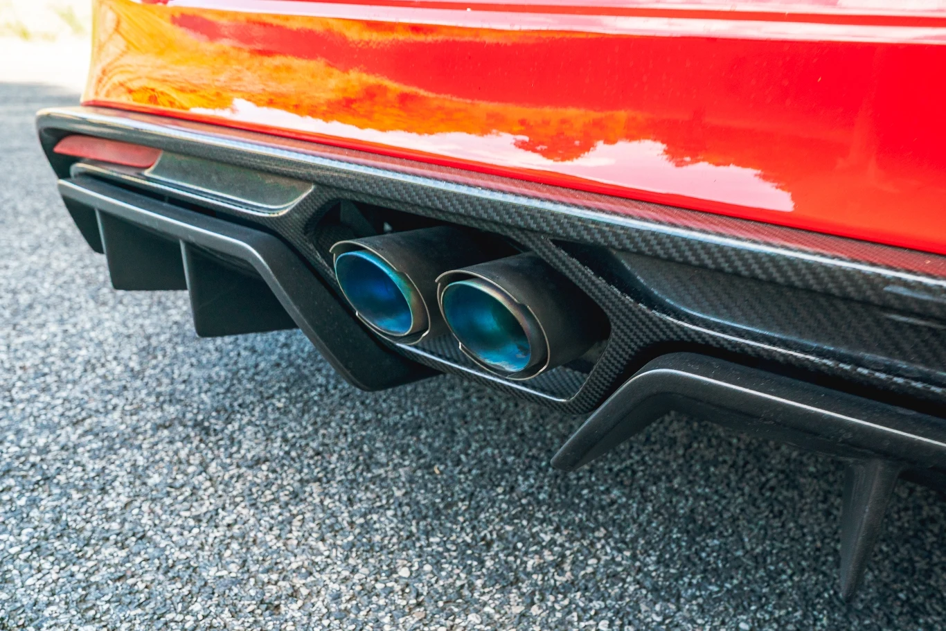 Opcjonalny wydech Akrapovica brzmi doskonale, ale wymaga dopłaty 17 400 zł Podwójny wydech sportowego samochodu z wykończeniem z włókna węglowego, widoczny na tle asfaltowej drogi, światło odbija się od czerwonego lakieru nadwozia.