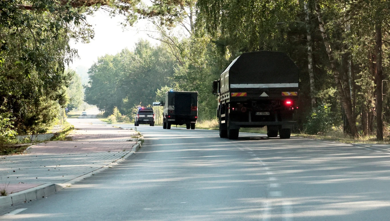 W trzech miejscach odnaleziono szczątki obiektów przypominających drony, zdj. ilustracyjne Kolumna wojskowych pojazdów jadących asfaltową drogą przez zalesiony teren w słoneczny dzień, otoczonych zielenią i cieniem drzew.