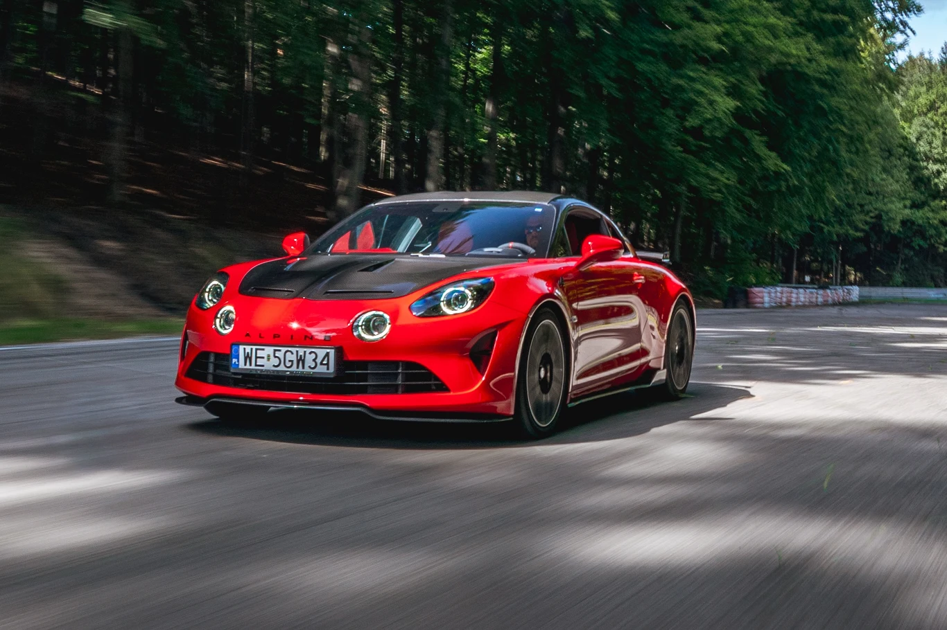Alpine A110 R Czerwony sportowy samochód jadący dynamicznie po krętej asfaltowej drodze w lesie, w tle drzewa i rozmazany asfalt podkreślający ruch pojazdu