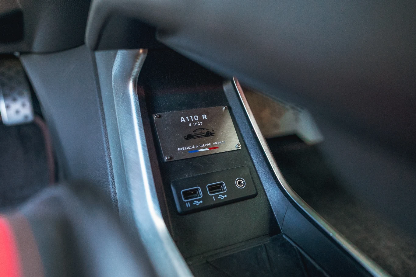 Alpine A110 R Centralny panel samochodu z widoczną tabliczką znamionową A110 R, dwoma gniazdami USB i detalami wnętrza pojazdu sportowego.