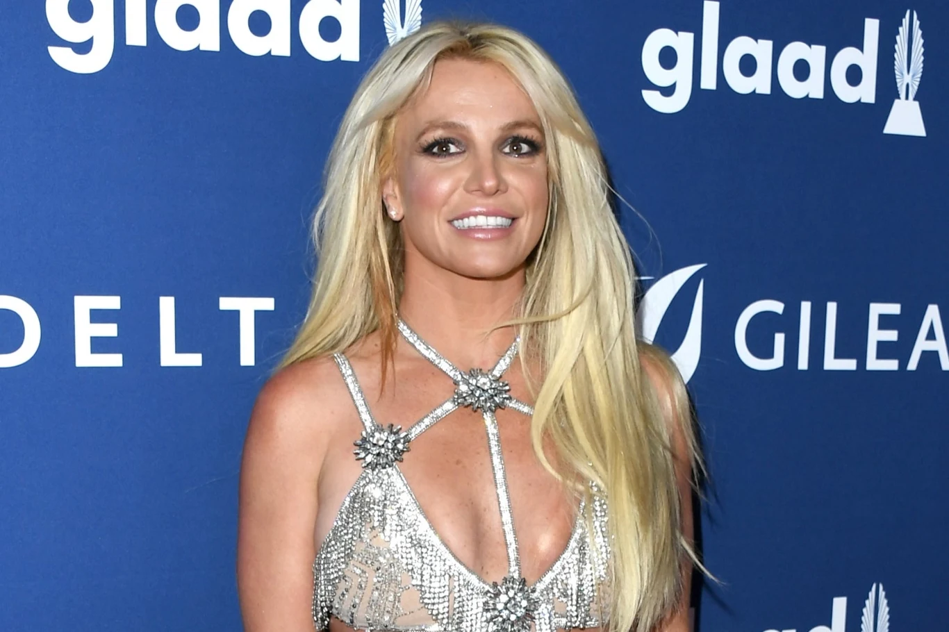 Britney Spears od pewnego czasu stara się naprawić relację z synami Kobieta o długich blond włosach ubrana w błyszczącą suknię z odkrytymi ramionami, stoi na tle niebieskiej ściany z widocznymi logotypami organizacji i sponsorów.