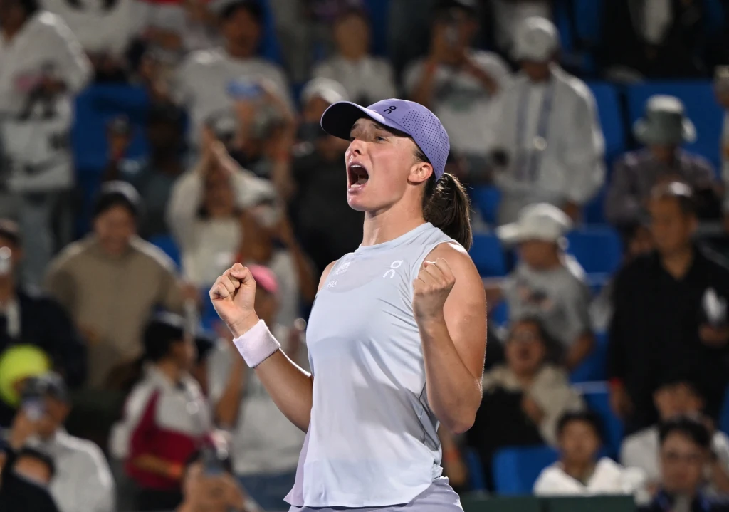 Iga Świątek Zawodniczka tenisowa w sportowym stroju, stojąca na korcie z uniesionymi pięściami i wyrażająca silne emocje po wygranym punkcie, w tle rozmyta publiczność dopingująca na trybunach.