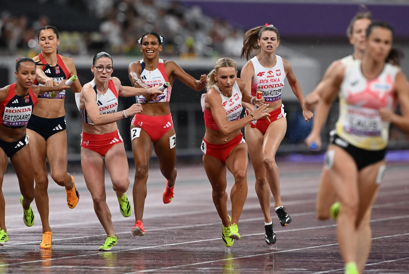 Justyna Święty-Ersetic Sztafeta kobiet podczas zawodów lekkoatletycznych, zawodniczki w trakcie przekazywania pałeczki, na bieżni stadionu w dynamicznym ruchu, energia, rywalizacja sportowa.
