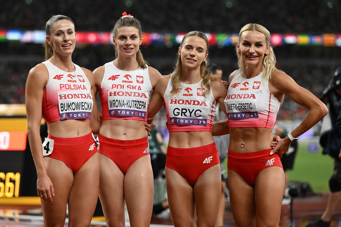 Od lewej: Natalia Bukowiecka, Alicja Wrona-Kutrzepa, Anna Gryc i Justyna Święty-Ersetic Cztery polskie lekkoatletki w strojach sportowych stoją obok siebie na stadionie, uśmiechnięte, z widocznymi nazwiskami na koszulkach oraz oznaczeniami sponsorów, w tle rozmyta widownia i stadionowe światła.