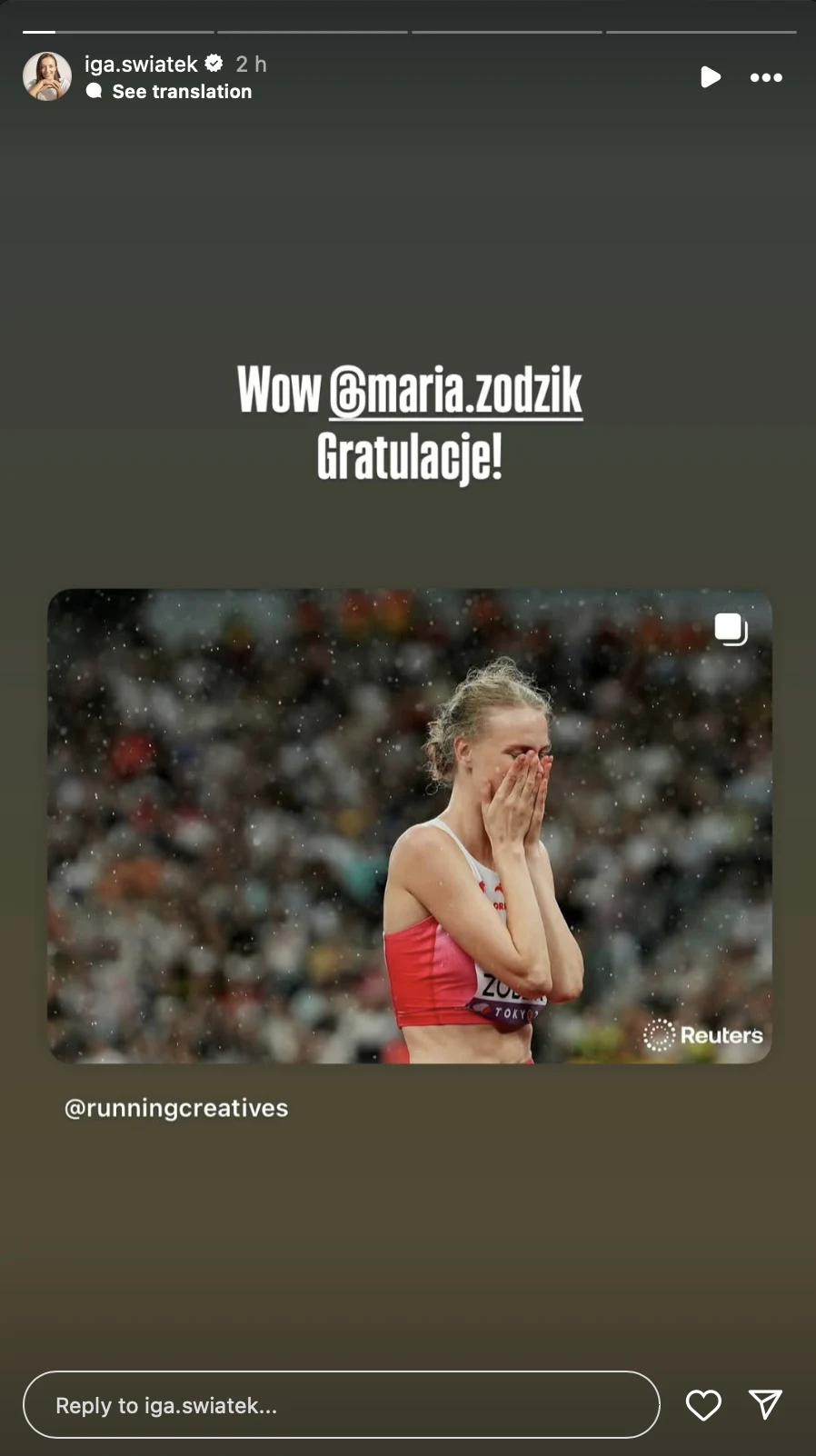 Zawodniczka lekkoatletyczna w czerwonym stroju trzyma dłoń na ustach, wyrażając silne emocje, prawdopodobnie ze wzruszenia lub radości, tłum w tle jest rozmyty.