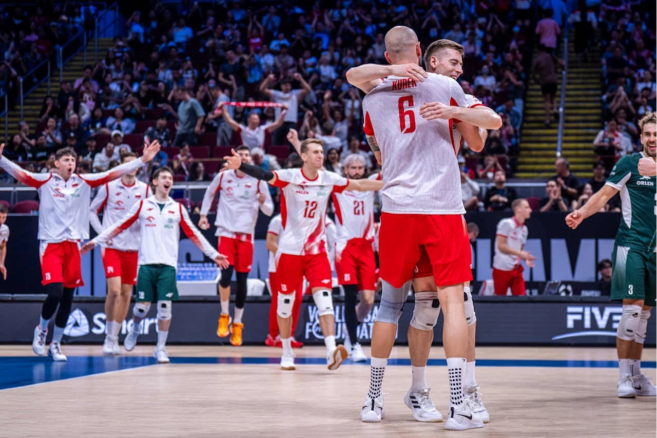 Polscy siatkarze cieszący się z wygranej na zakończonym meczu, obejmują się na środku boiska, w tle widoczna rozemocjonowana publiczność oraz pozostali zawodnicy drużyny.