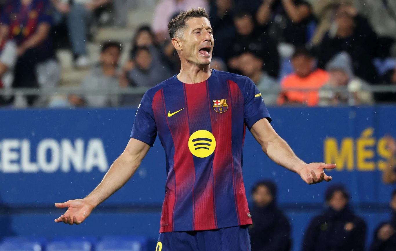 Piłkarz w barwach FC Barcelony z uniesionymi rękami w geście niezadowolenia na tle stadionu i widowni.