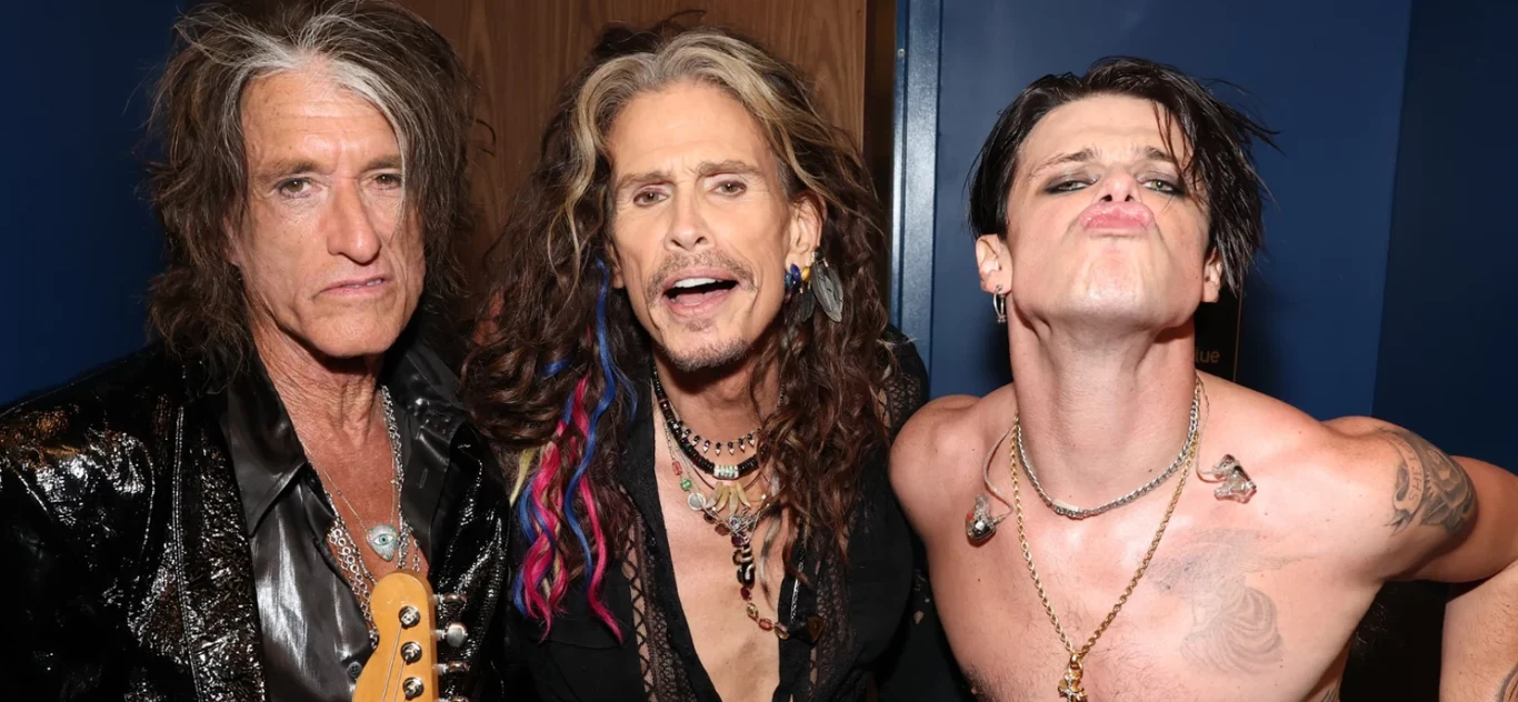 Joe Perry i Steven Tyler z Aerosmith i Yungblud podczas gali MTV Video Music Awards 2025 Trzech mężczyzn w charakterystycznych, rockowych stylizacjach pozuje razem, środkowy mężczyzna ma długie włosy i naszyjniki, po prawej osoba z rozrzuconymi włosami wypina usta, bez koszulki, ozdobiona tatuażami i biżuterią.