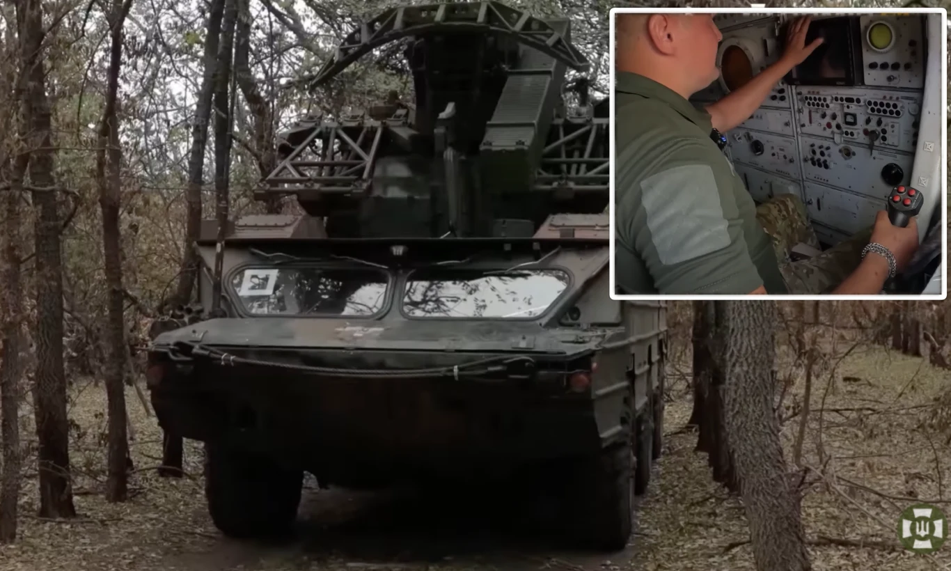 Polska Osa-AKM-P1 "Żądło" gamechangerem w walce z rosyjskimi dronami i nie tylko Samobieżny system rakietowy w otoczeniu lasu, w prawym górnym rogu widoczny operator przy panelu sterowania, wokół pojazdu gęste drzewa i sucha roślinność.