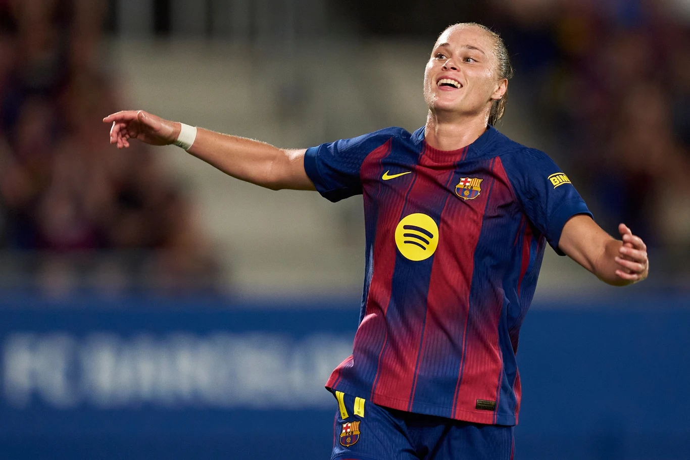 Ewa Pajor Piłkarka w stroju FC Barcelony podczas meczu, z szerokim uśmiechem na twarzy, z uniesionymi ramionami, na tle rozmazanej trybuny stadionu.