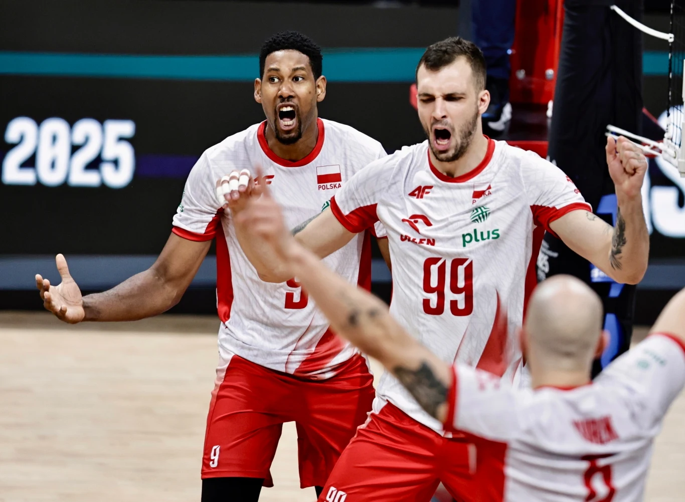 Grupa siatkarzy w biało-czerwonych strojach drużyny narodowej Polski wyraża silne emocje po zdobyciu punktu podczas meczu, na pierwszym planie widoczne dynamiczne gesty rąk i radość zawodników.