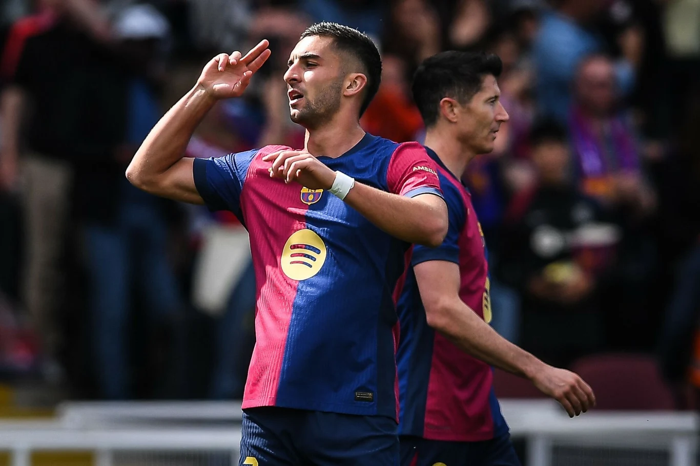 Dwóch piłkarzy w strojach meczowych cieszy się po zdobyciu gola na tle rozmazanej publiczności na stadionie sportowym.