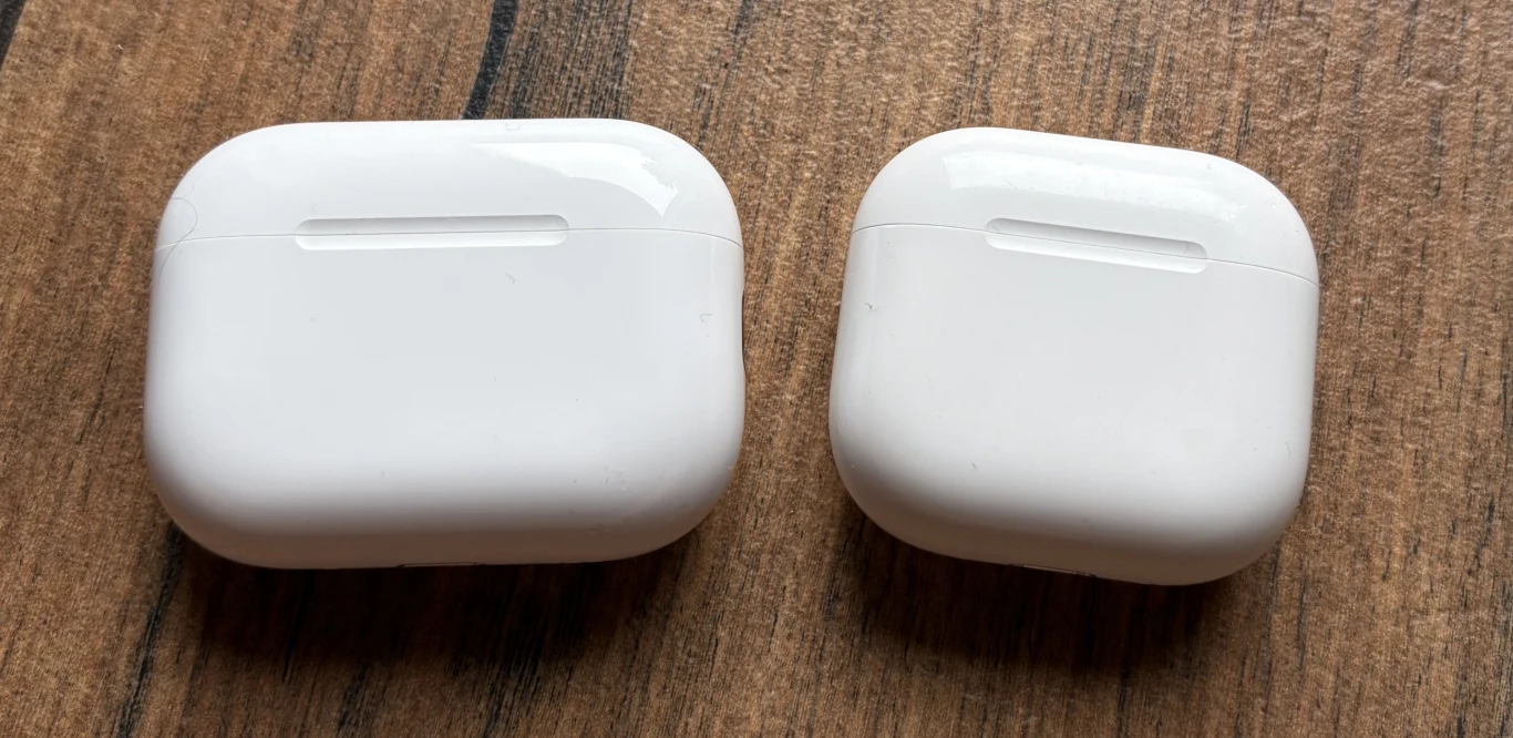 Dwa białe etui na słuchawki bezprzewodowe leżące obok siebie na drewnianej powierzchni, jedno z nich jest większe od drugiego.