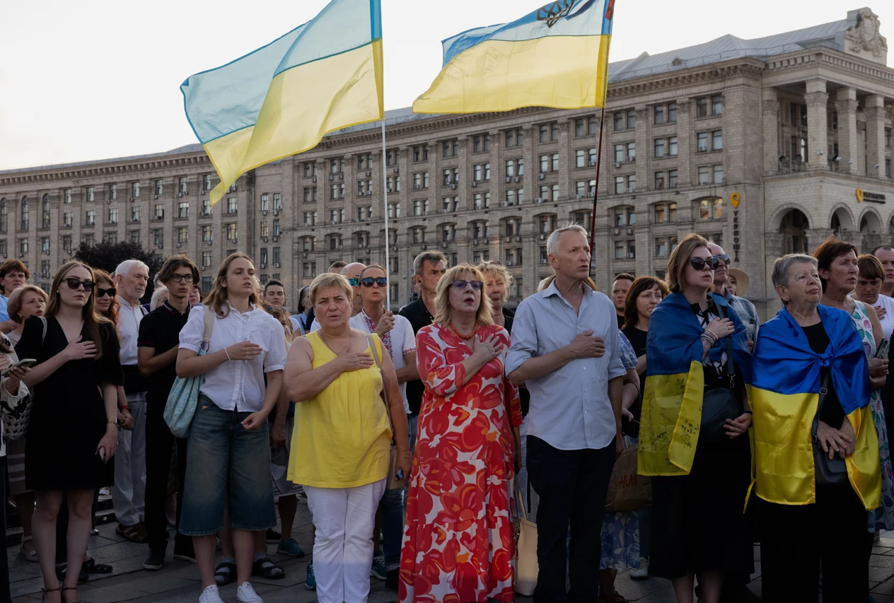 Nowy sondaż wskazuje, że zdecydowana większość Ukraińców nie chce opuszczać kraju Grupa ludzi stoi razem na tle dużego budynku, wiele osób ma przyłożoną rękę do serca, dwie osoby trzymają flagi Ukrainy, kilka osób jest ubranych w niebiesko-żółte kolory odpowiadające barwom narodowym.