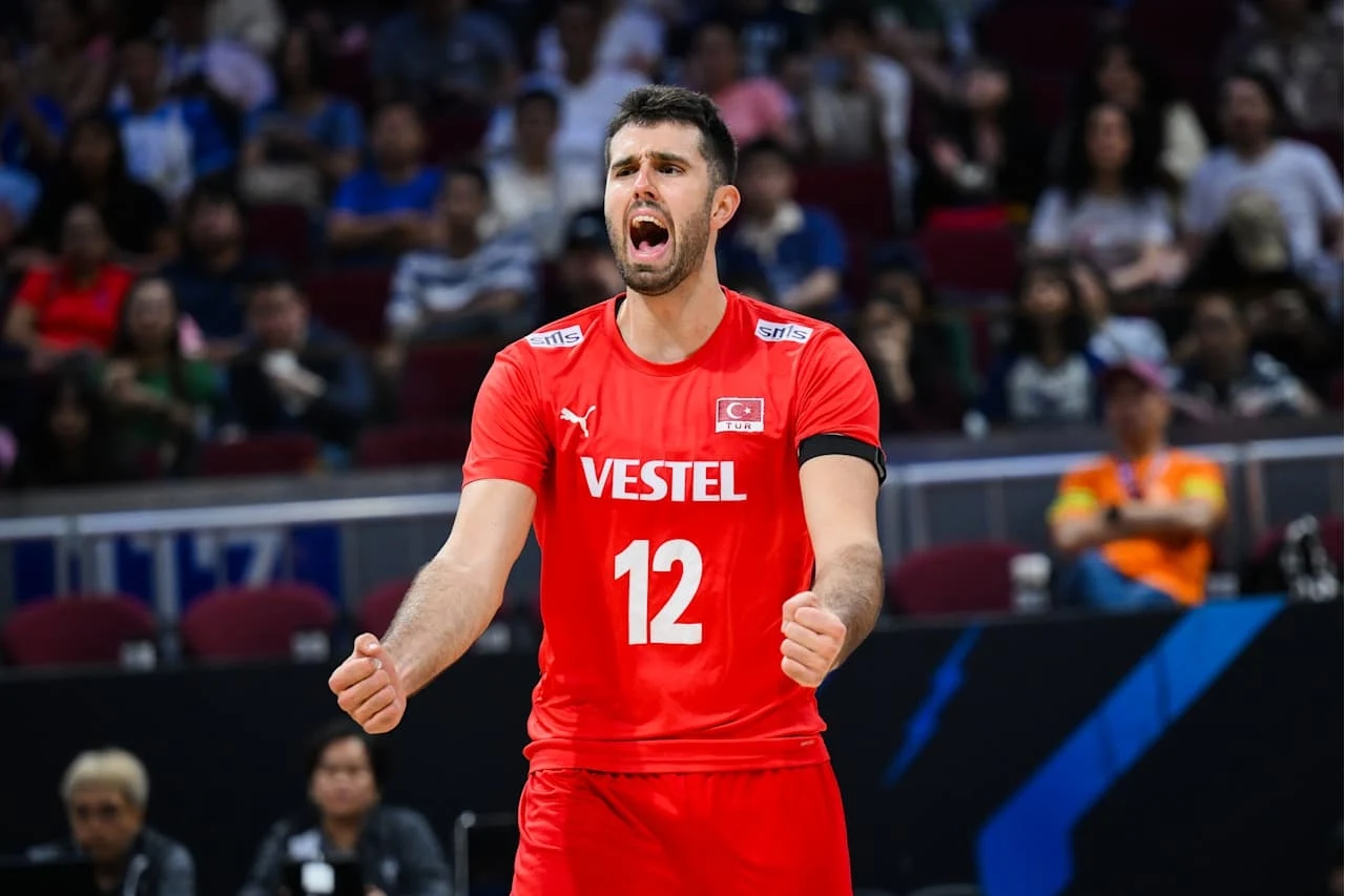 Adis Lagumdzija Siatkarz w czerwonym stroju z numerem 12 i flagą Turcji na koszulce okazuje emocje podczas meczu, w tle widownia na hali sportowej.