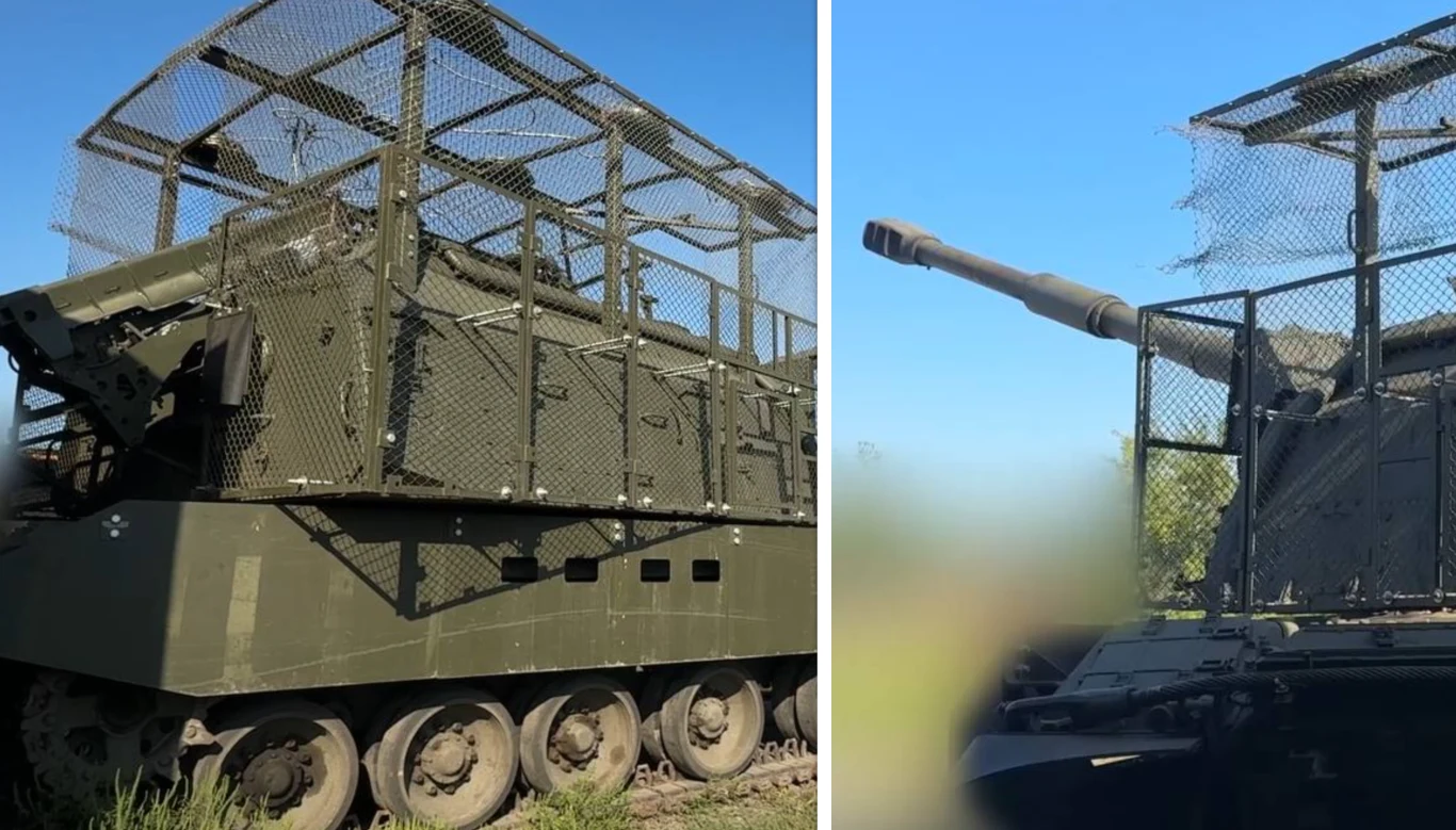 Sami Rosjanie nazywają je "grillami". 2S19M2 Msta-S z nową klatką bezpieczeństwa Samobieżna armatohaubica wojskowa w zielonym kamuflażu, osłonięta dodatkową konstrukcją z metalowej siatki oraz paneli ochronnych, ustawiona na otwartym terenie pod niebieskim niebem.