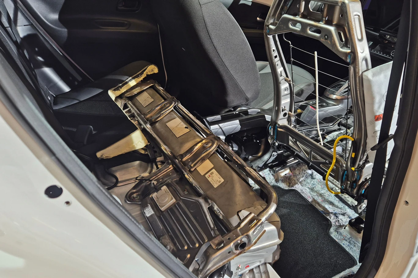 Wnętrze samochodu z widocznymi elementami rozebranego tylnego siedzenia oraz baterii trakcyjnej, charakterystycznej dla pojazdów hybrydowych lub elektrycznych.