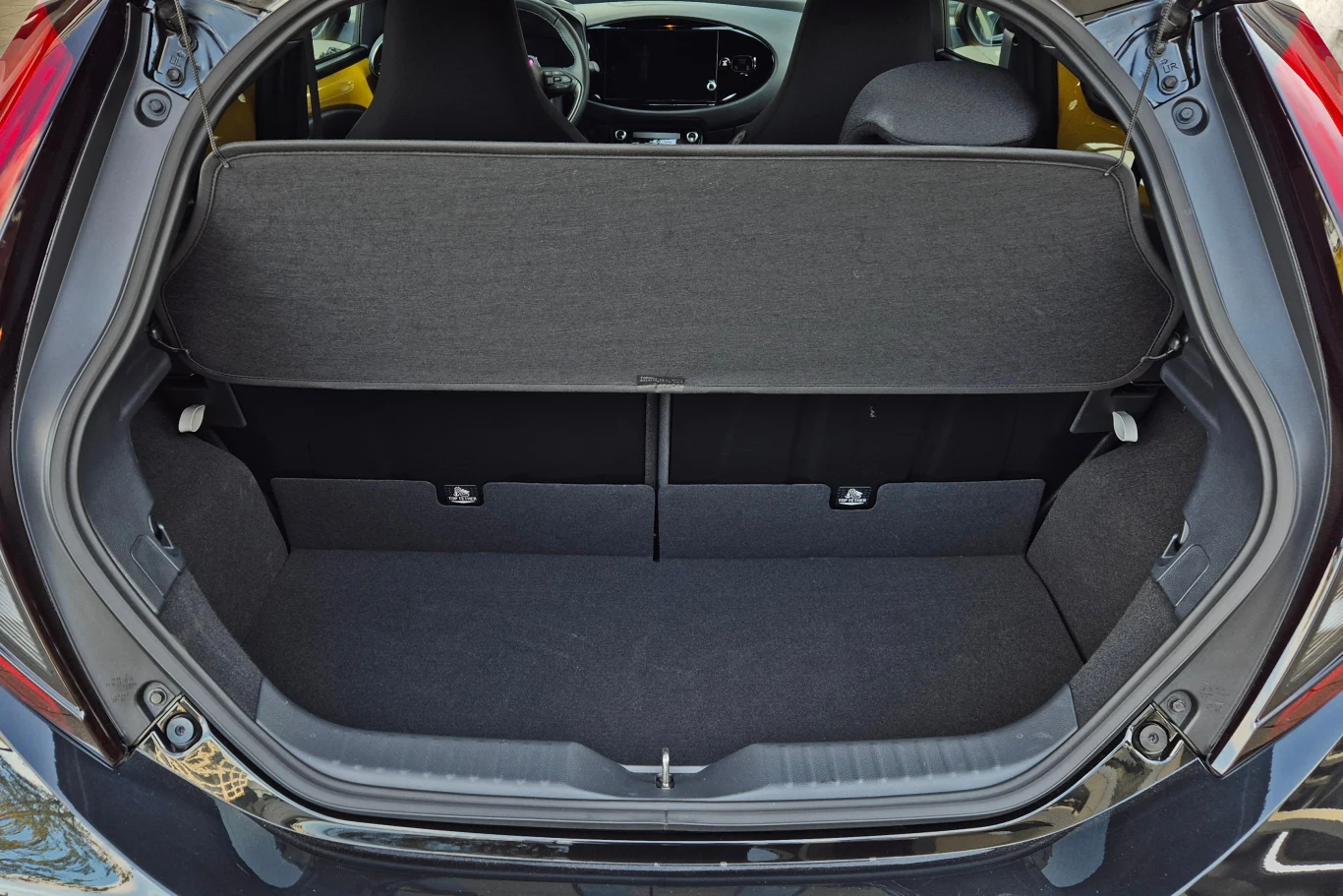 Wnętrze bagażnika samochodu osobowego z widoczną półką bagażową, siedzeniami oraz czystą, pustą przestrzenią bagażową.