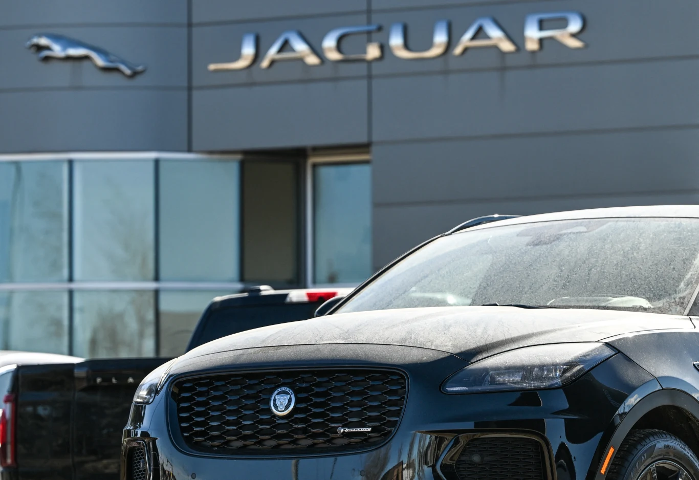 Jaguar wstrzymuje produkcję po cyberataku Czarny samochód marki Jaguar zaparkowany przed budynkiem salonu samochodowego z wyraźnym logo Jaguar na elewacji.